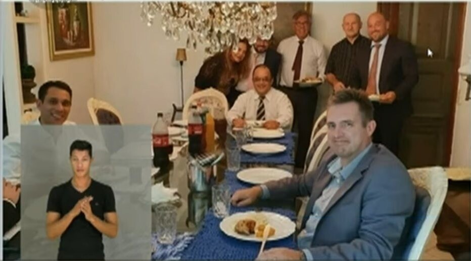 Sentados à mesa estão três homens brancos de roupa social; em pé está uma mulher à esquerda e outros quatro homens brancos de roupa social à sua direita
