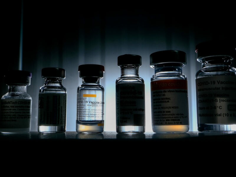 Posicionados contra à luz, estão seis frascos diferentes de vacina