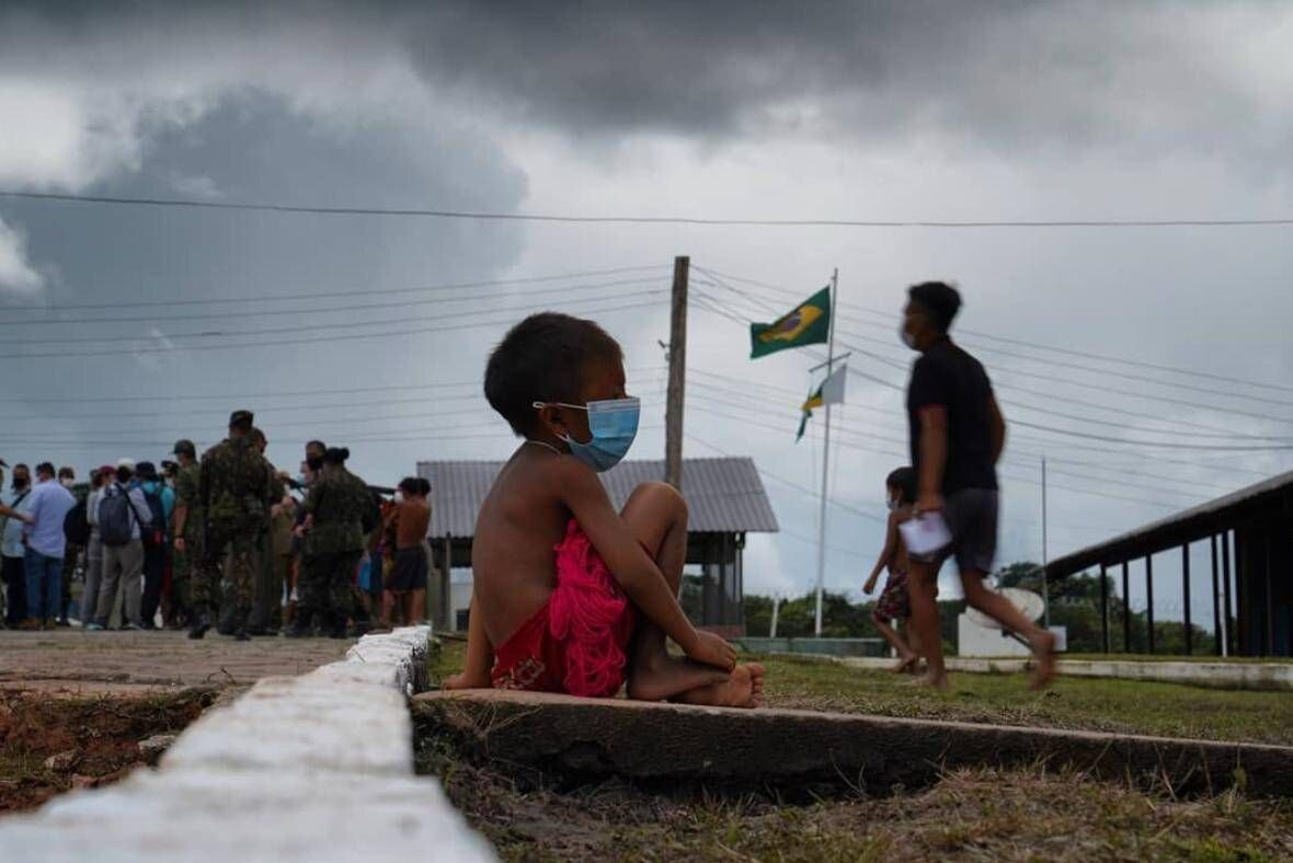 Criança indígena à beira da estrada com exército e bandeira do Brasil ao fundo