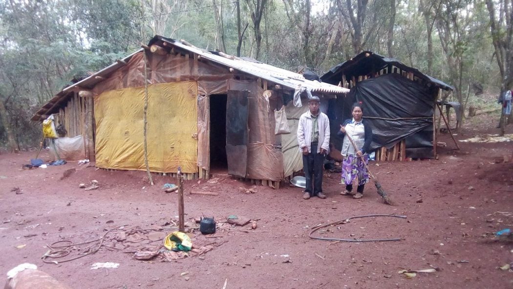 Na foto, um acampamento indígena com duas construções feitas com madeira, plástico e lona; com condições insalubres, eles vivem em meio à miséria