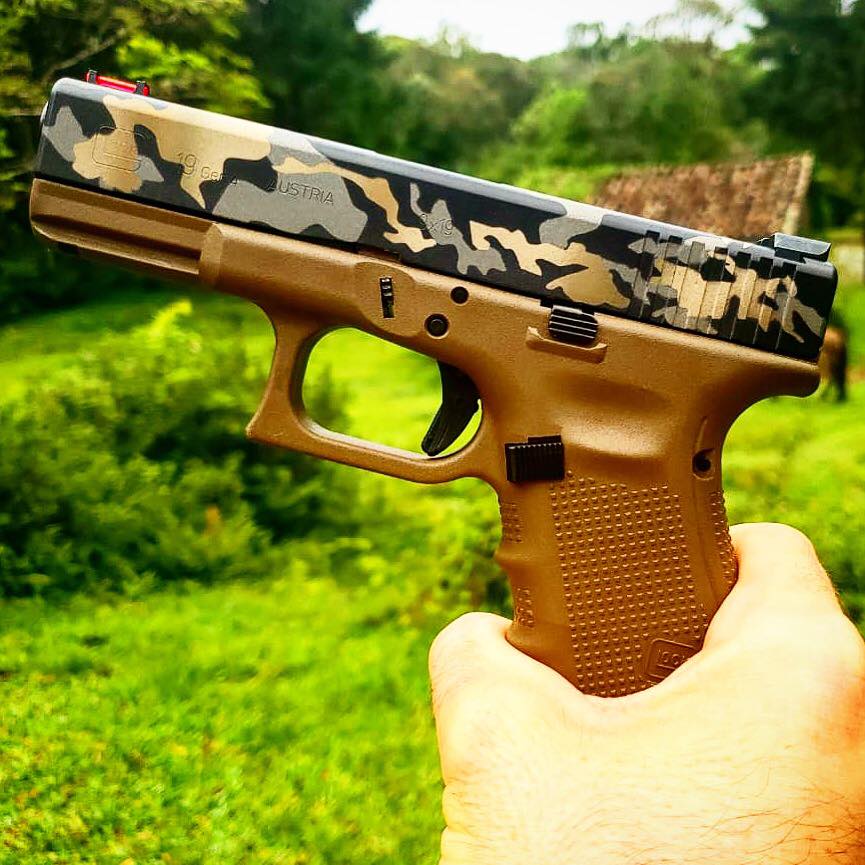 Na foto, uma arma da Glock dourada com o cano em estampa camuflada.