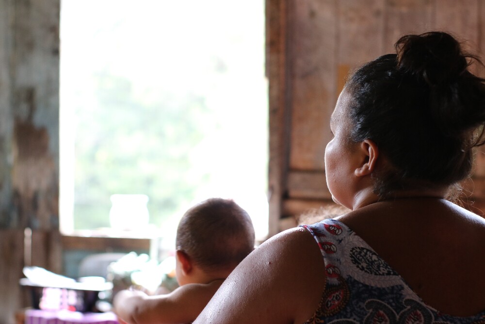 Uma mulher negra posa de costas para a câmera; ela segura um bebê