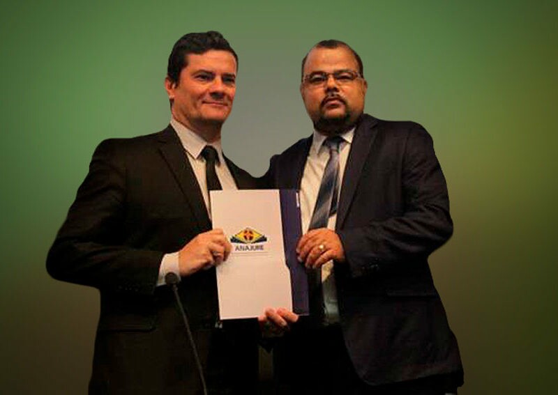 Sergio Moro e Uziel Santana, da esquerda para a direita, seguram juntos um documento; ambos vestem ternos na cor preta