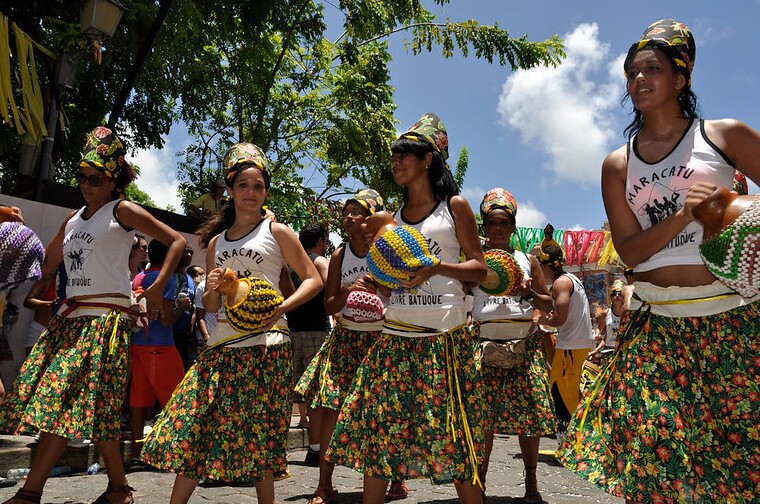 Foliões desfilam durante festejo de maracatu em Olinda, segurando instrumentos típicos nas mãos