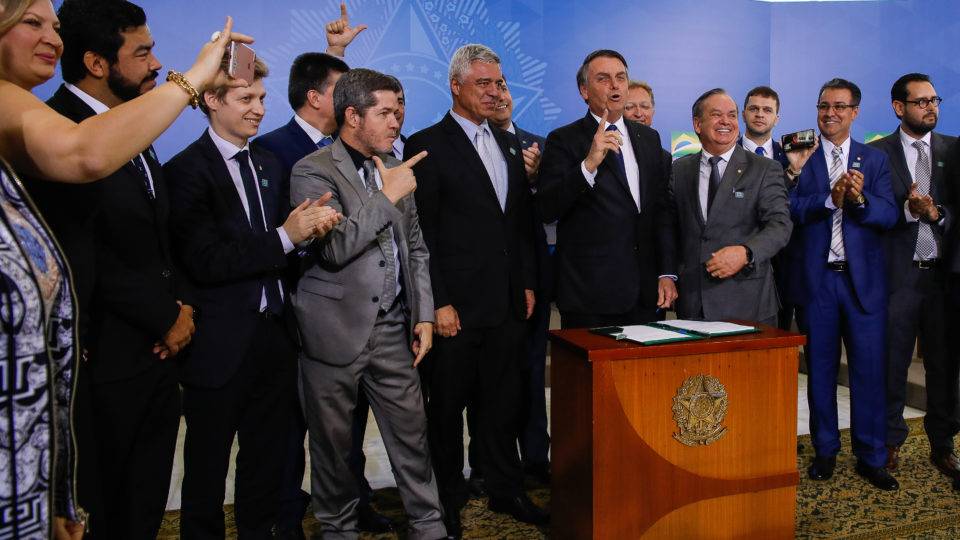 O presidente Jair Bolsonaro está acompanhado de alguns homens e mulheres que fazem o sinal de arminha com as mãos, durante evento sobre posse e porte de arma