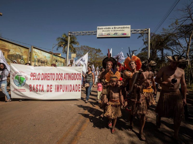 Manifestantes andam por rua em Minas Gerais e seguram faixa branca com os dizeres em vermelho "Pelo direitos dos atingidos" e "Basta de impunidade"