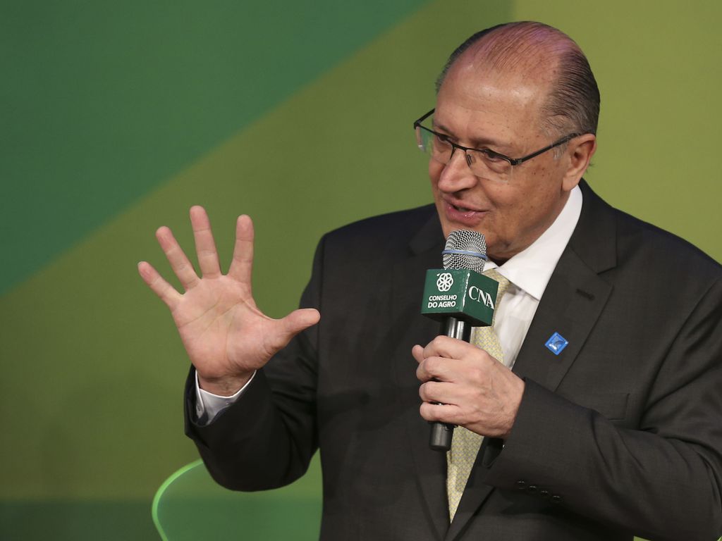 Alckmin é um homem branco, calvo e com olhos castanhos; ele veste terno preto e óculos