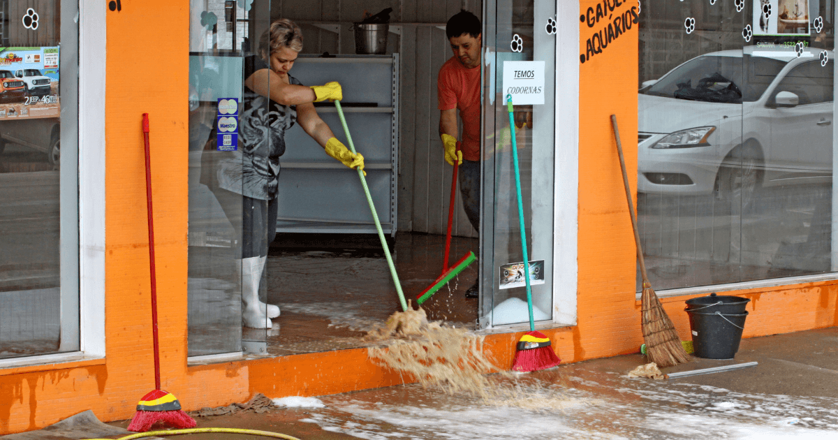 Homem e mulher puxam água com rodo de comércio na região de SC, após enchente
