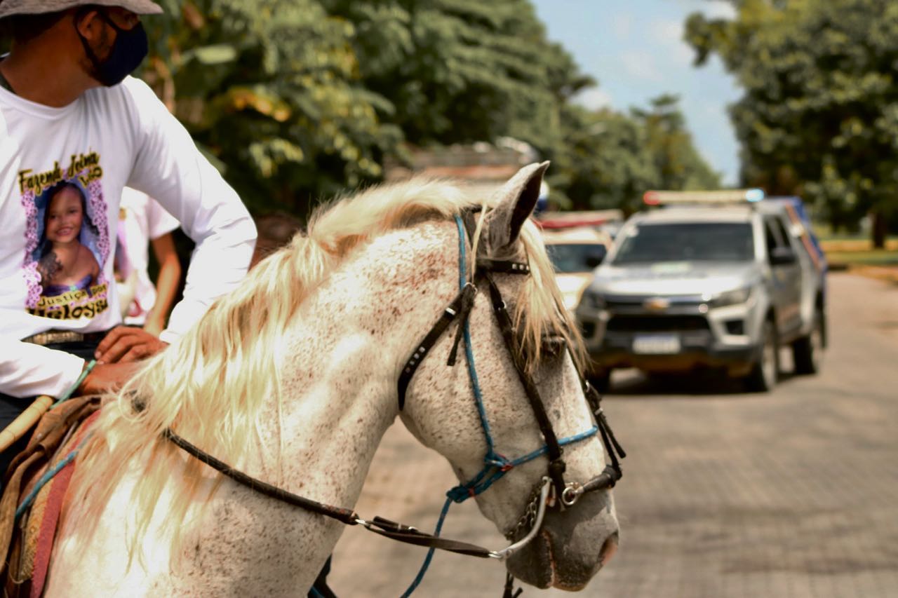 Imagem mostra homem com camiseta branca com a foto de Heloysa, andando a cavalo durante protesto contra o assassinato da criança