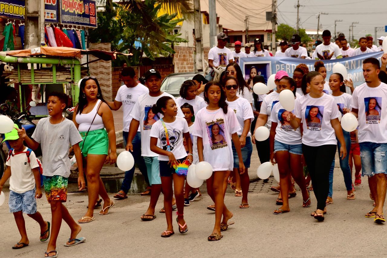 Dezenas de moradores caminham em memória de Heloysa; eles vestem camisetas brancas com a sua foto e seguram balões e faixas