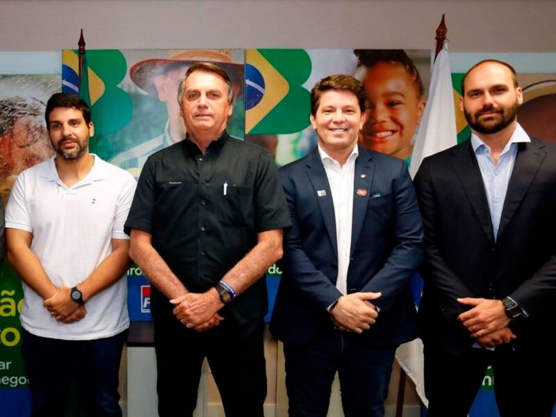 Na imagem é possível ver André (à esq), Bolsonaro (ao lado), Mário (ao lado) e Eduardo Bolsonaro (à direita). Todos são homens brancos e estão com as mãos cruzadas diante do corpo.