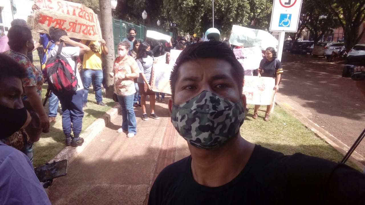 Hernâni Cáceres é um homem indígena com cabelos e olhos castanhos; ele veste uma camiseta preta e uma máscara facial estampada