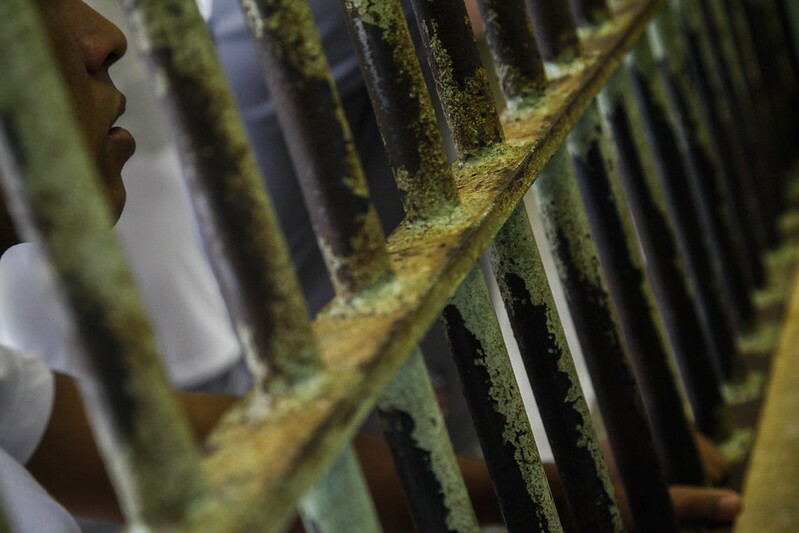 Imagem mostra perfil de homem entre grades de uma penitenciária