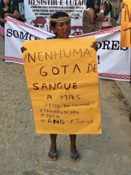 Mulher indígena do Vale do Javari segura cartaz com os dizeres "nenhuma gota de sangue a mais"