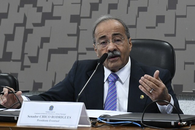 Senador Chico Rodrigues é um homem na faixa dos 60 anos, com cabelos e bigode grisalhos; ele veste terno preto com camisa branca e gravata azul