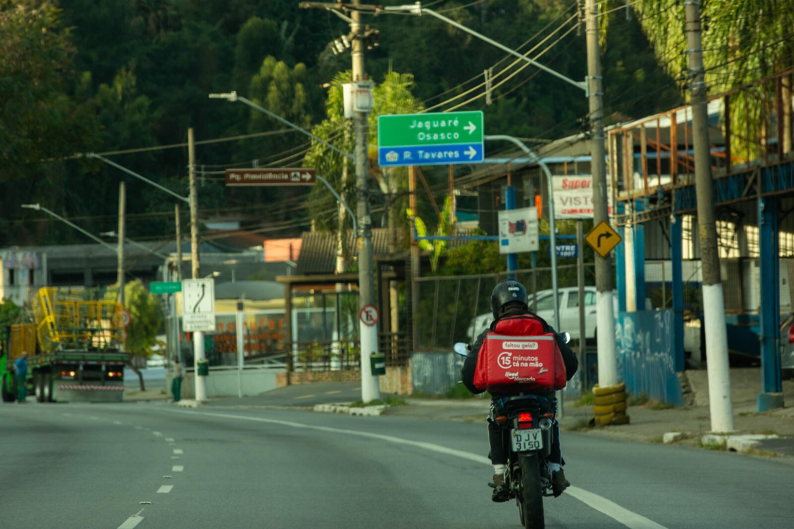 Motoboy percorre rua de São Paulo com mochila vermelha do iFood nas costas