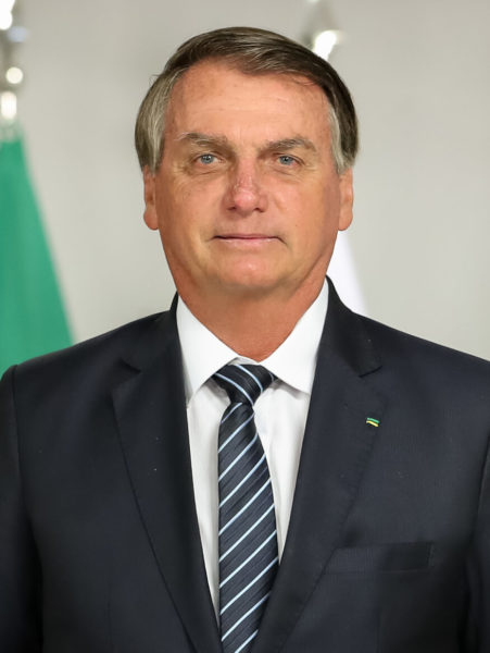 Na imagem o presidente Jair Bolsonaro. Bolsonaro é um homem branco com cabelos grisalhos e olhos claros, ele usa terno azul escuro e gravata na mesma cor com listras azul claro.