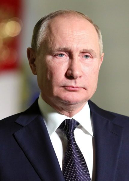 Na imagem o presidente da Rússia Vladimir Putin. Putin é um homem branco, calvo, com olhos claros, na imagem ele veste terno preto e gravata roxa.