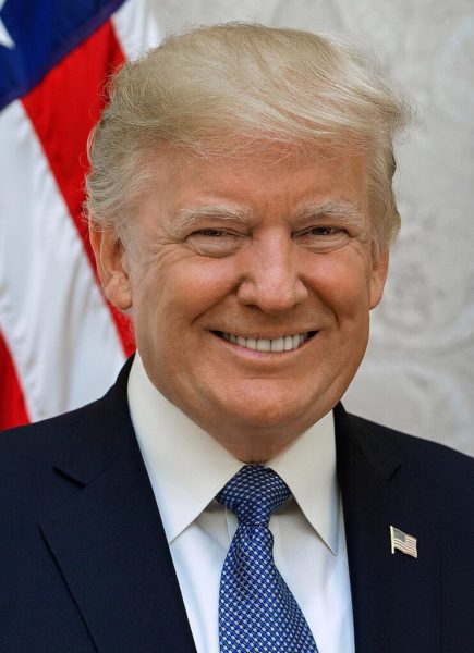 Na imagem, o ex presidente dos Estados Unidos Dolnald Trump. Trump é um homem branco de meia idade com cabelos loiros e olhos claros, ele usa terno preto e gravata azul.