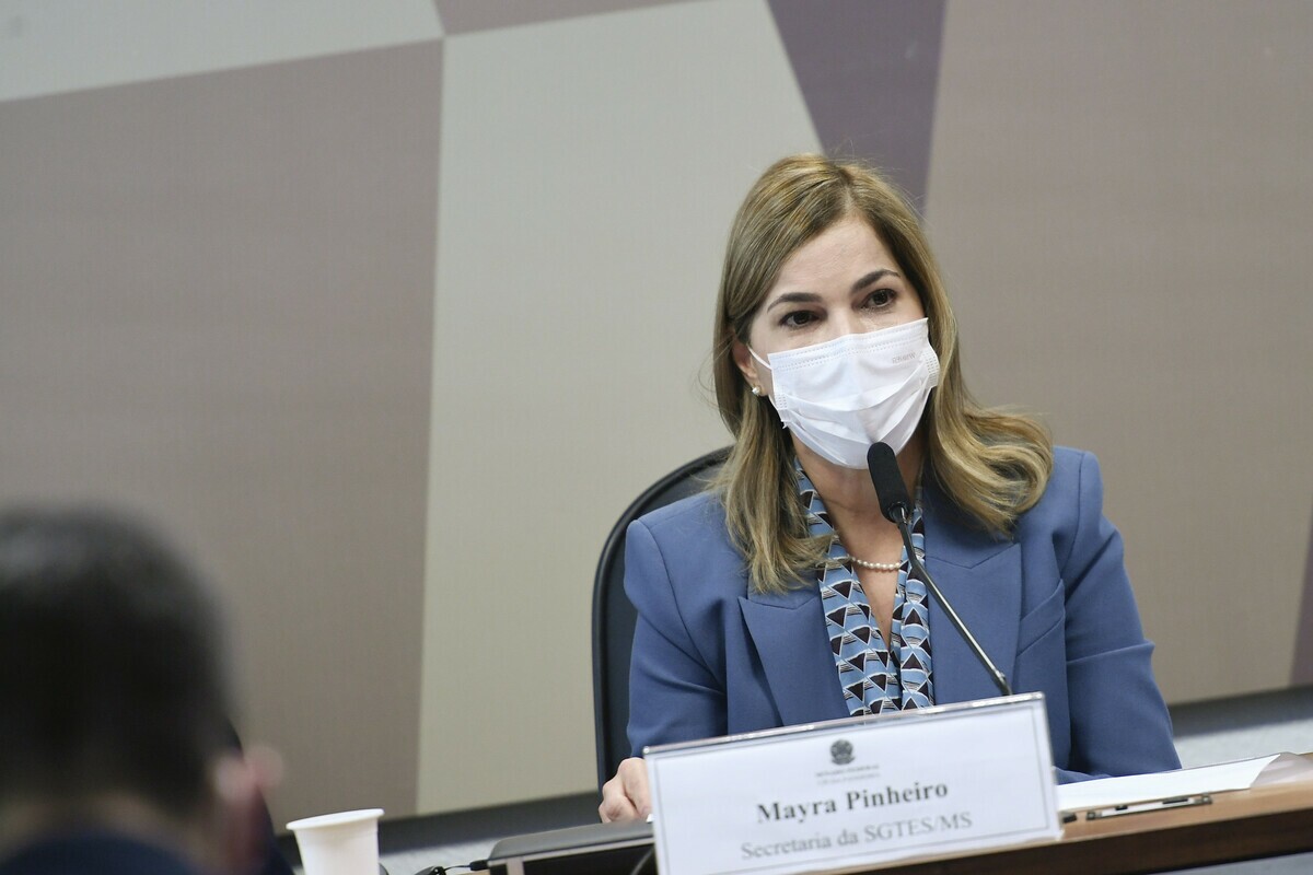 Mayra Pinheiro é uma mulher branca com cabelos loiros e olhos castanhos. Mayra veste casaco azul claro e camisa estampada.