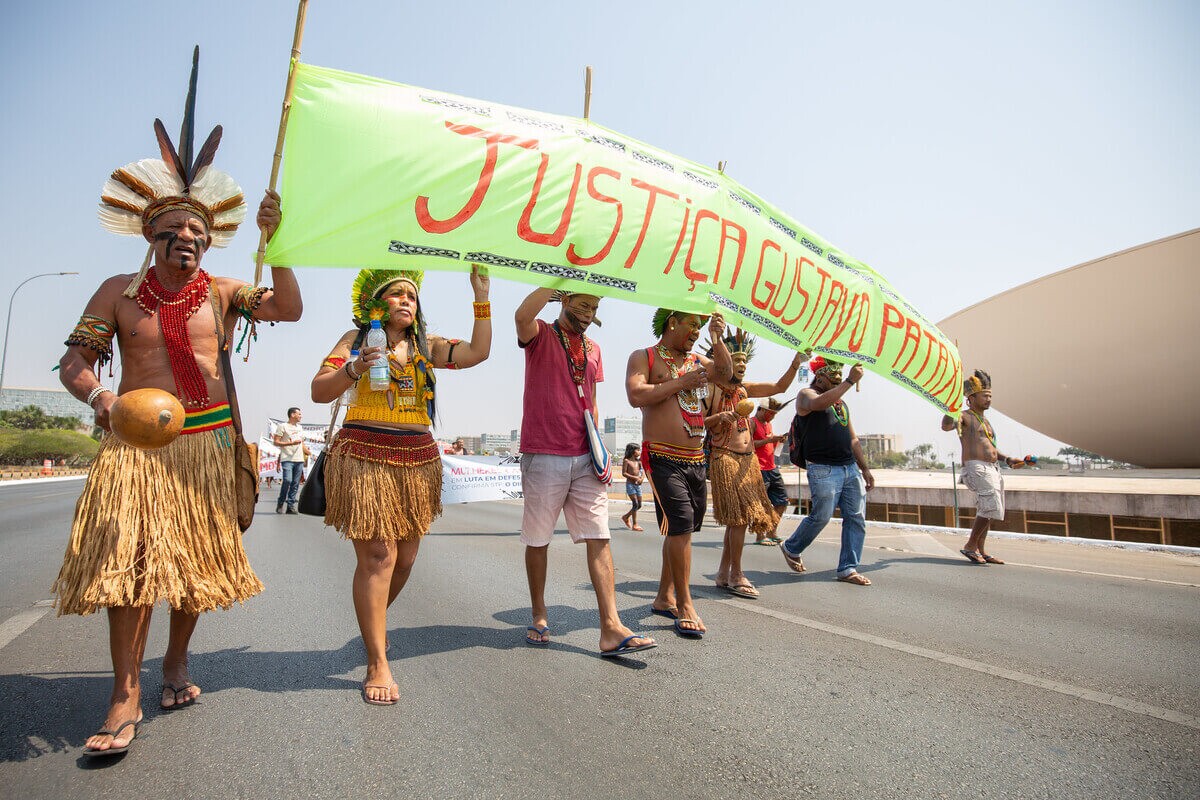 Indígenas Pataxó protestam na Praça dos Três Poderes com trajes típicos carregando faixa dizendo ''Justiça Gustavo Pataxó''