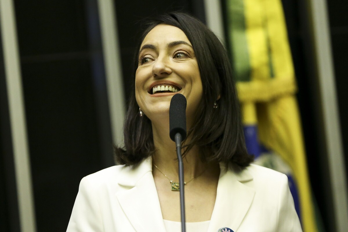 Rosângela Moro deputada federal eleita pelo União Brasil, é uma mulher branca com cabelos e olhos castanhos, ela veste um casaco branco e colar com a bandeira do Brasil.