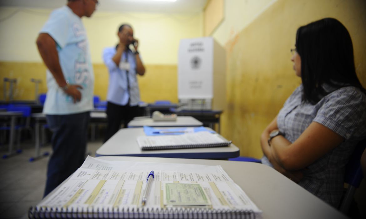 Mesários e eleitor em seção eleitoral durante votação.