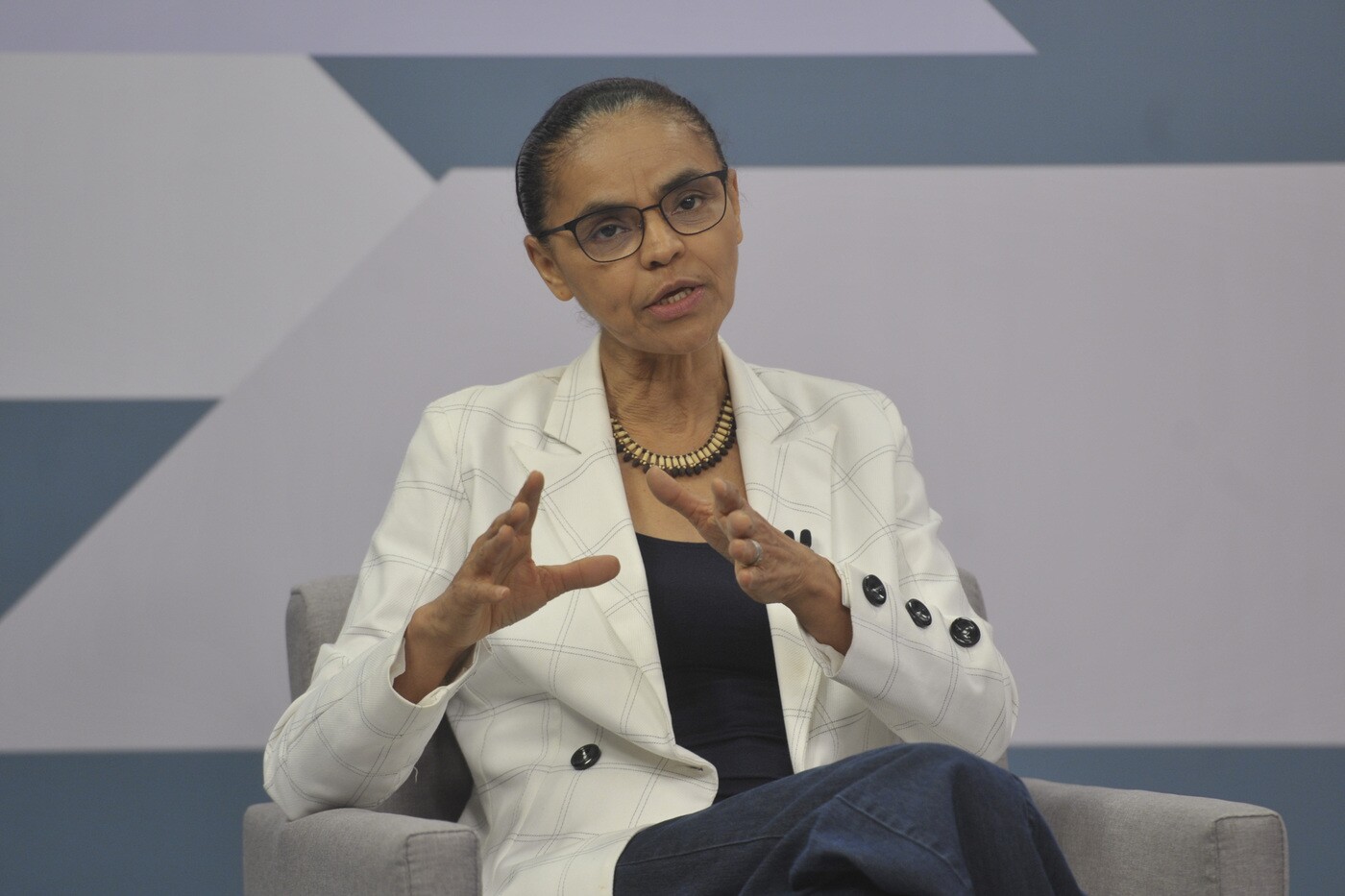 Na imagem, a deputada federal eleita Marina Silva (Rede-SP). Marina Silva é uma mulher negra com cabelos e olhos pretos na faixa dos 60 anos, ela usa blazer branco e colar de madeira.