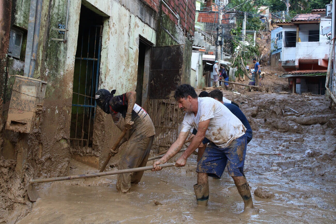 Homens trabalham tirando a lama de dentro de uma casa após as intensas chuvas do litoral norte de São Paulo