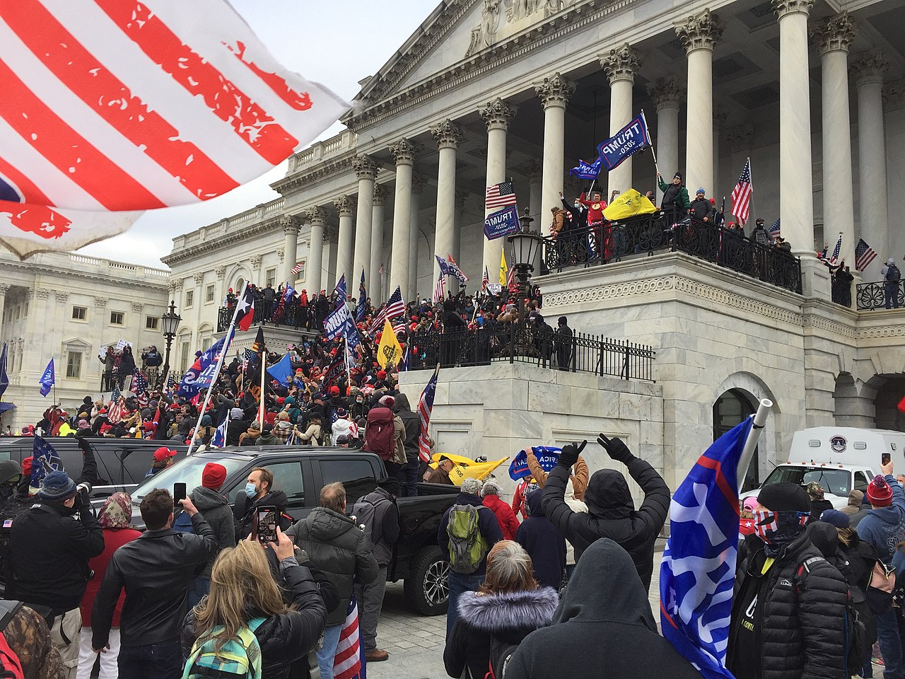 Trumpistas em frente ao capitólio protestam com bandeiras do ex presidente americano e bandeiras do Estados Unidos