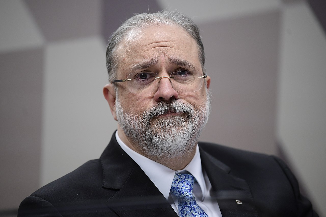 O procurador geral da república Augusto Aras é um homem branco com cabelos e barba grisalhos. Na imagem Aras usa óculos, terno e gravata azul estampada