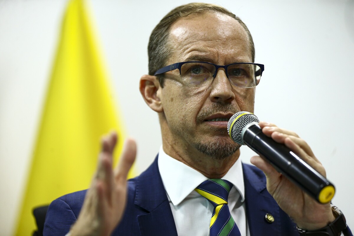 Ricardo Capelli é um homem branco com olhos e cabelos claros, na imagem usa óculos, terno azul e gravata com as cores da bandeira, ele fala ao microfone. Capelli foi ministro do GSI.