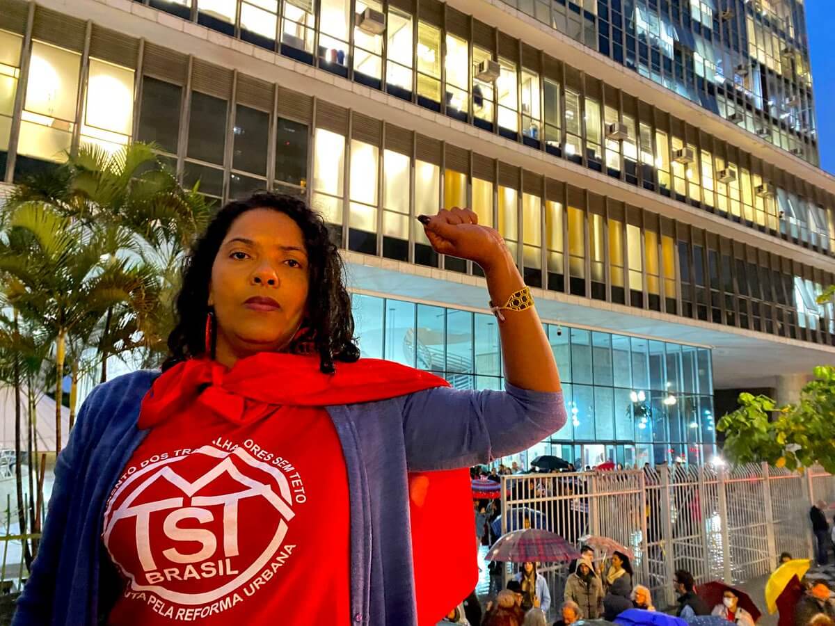 Debora Lima, militante do MTST, é uma mulher negra de cabelos escuros e cacheados. Ela está em um trio elétrico durante manifestação contra o Plano Diretor em São Paulo. Debora está com o punho levantado em sinal de resistência