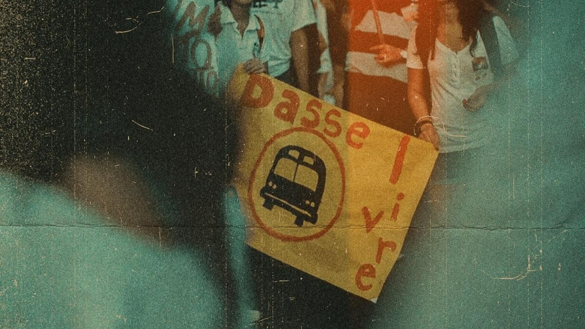 Manifestação contra o aumento da passagem dos transportes, na imagem duas pessoas seguram um cartaz com um ônibus desenhado escrito ''Passe Livre!''