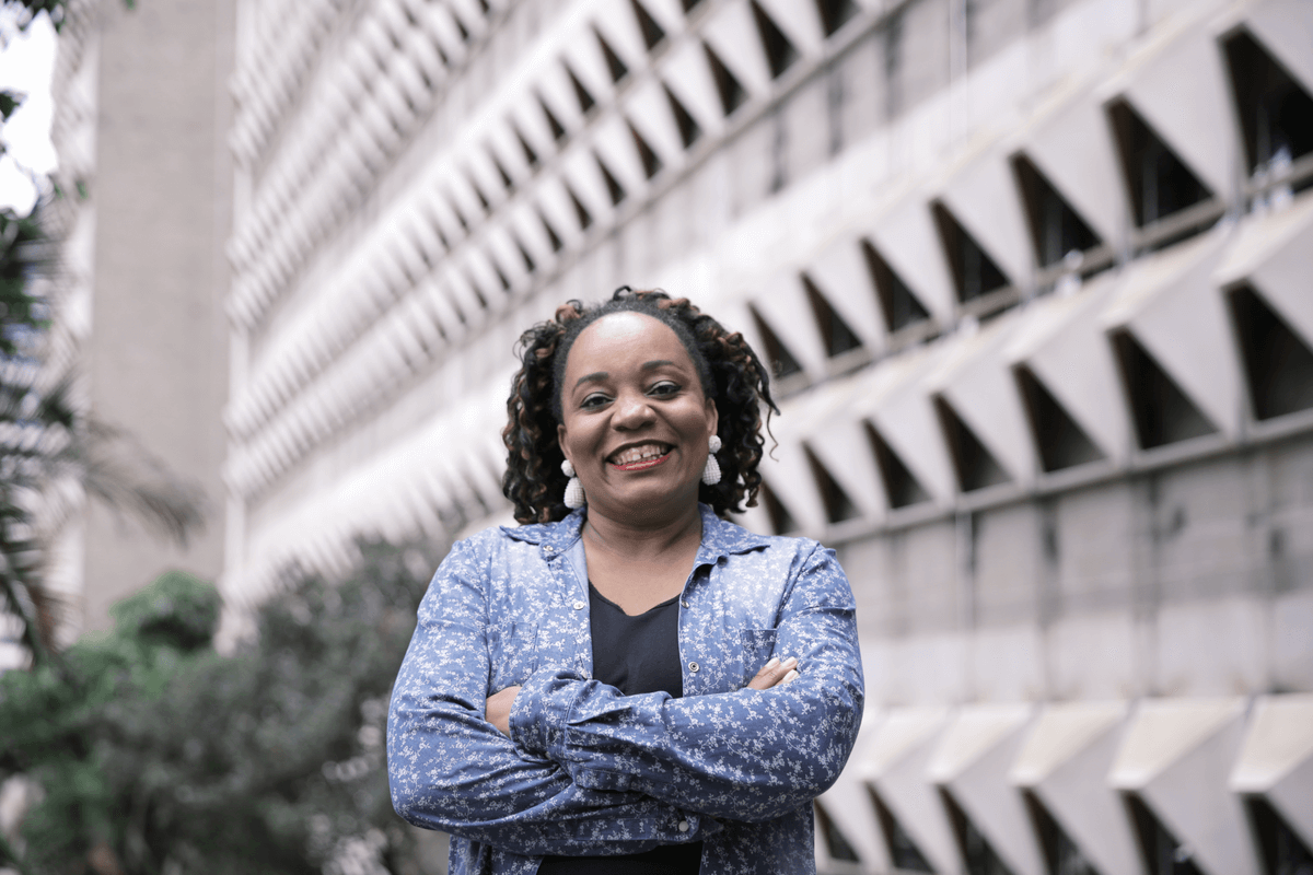 Priscila Cristina é uma mulher negra com cabelos castanhos e olhos escuros, Ela usa brincos de pérolas brancos e camisa estampada azul. Priscila Cristina formou-se em pedagogia pelo Prouni com bolsa de 100%.