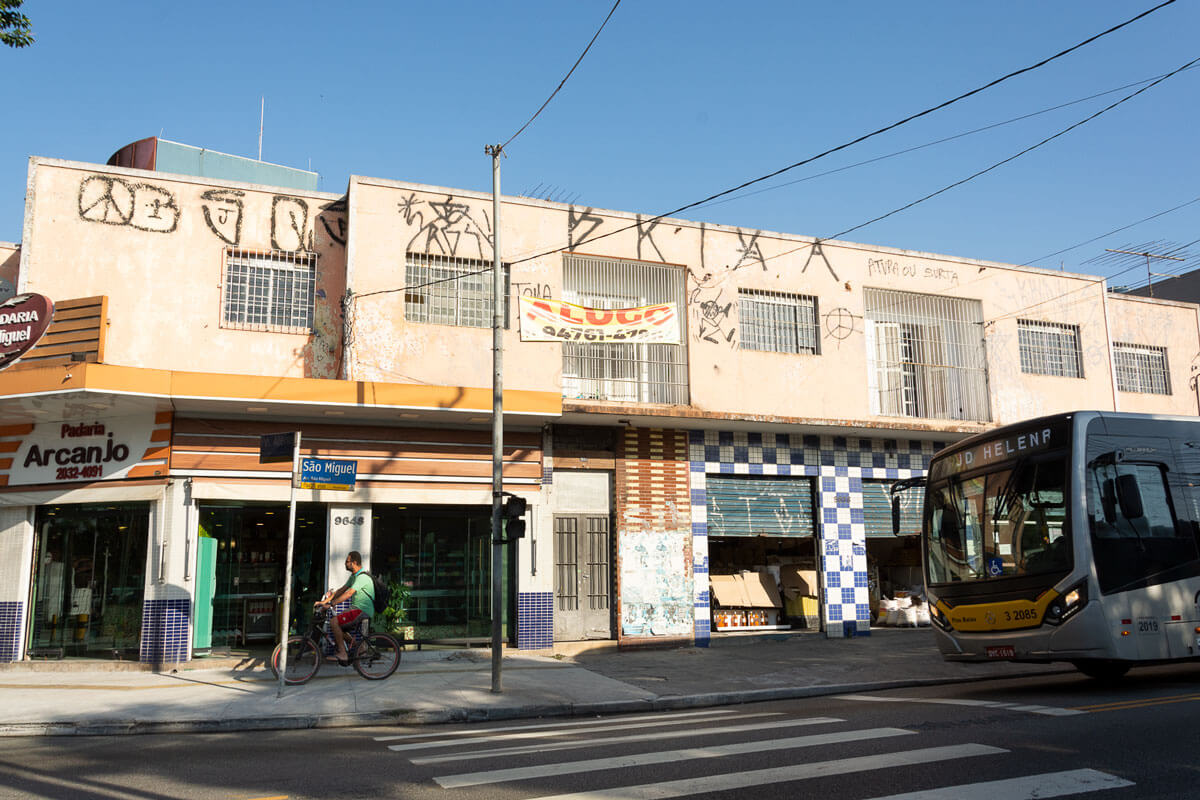 Esquina da Av. São Miguel, na imagem há uma padaria e em cima há um imóvel para disponível para aluguel.