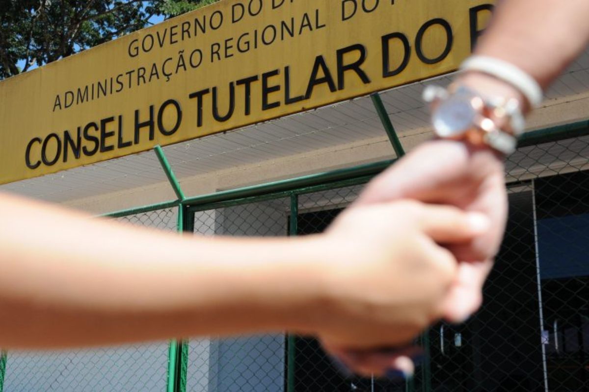 Mulher adulta segura a mão de uma criança em frente à fachada de uma unidade do conselho tutelar. Neste final de semana, 1 de outubro de 2023, tem eleição para os conselhos tutelares