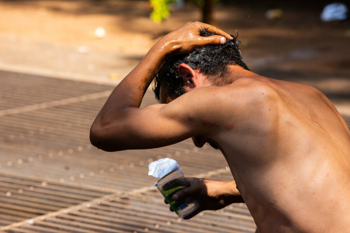 Pessoa em situação de rua uso copo de água para se refrescar durante onda de calor extremo em SP