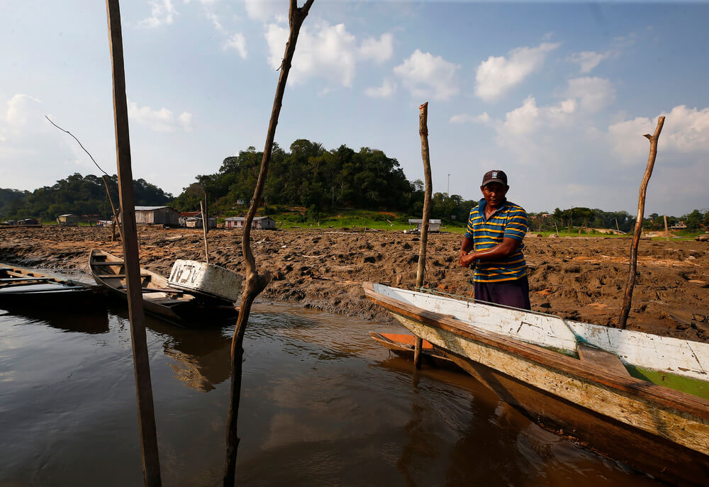 Pescador atraca barco na margem lamacenta do rio Solimões durante seca