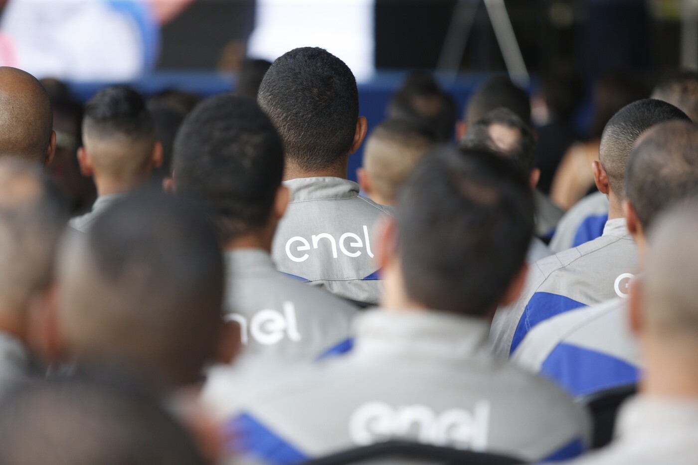 Imagem mostra funcionários da Enel de costas, com destaque para o logo da empresa no uniforme