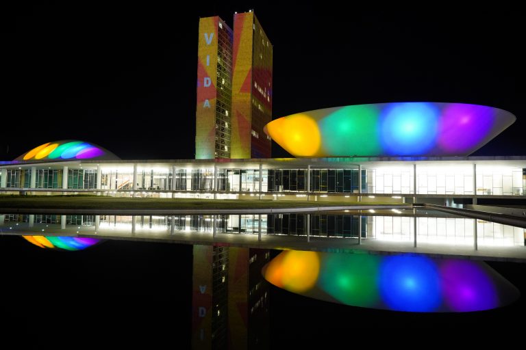 Imagem mostra cores da bandeira LGBTQIA+ refletida no prédio do Congresso em Brasília