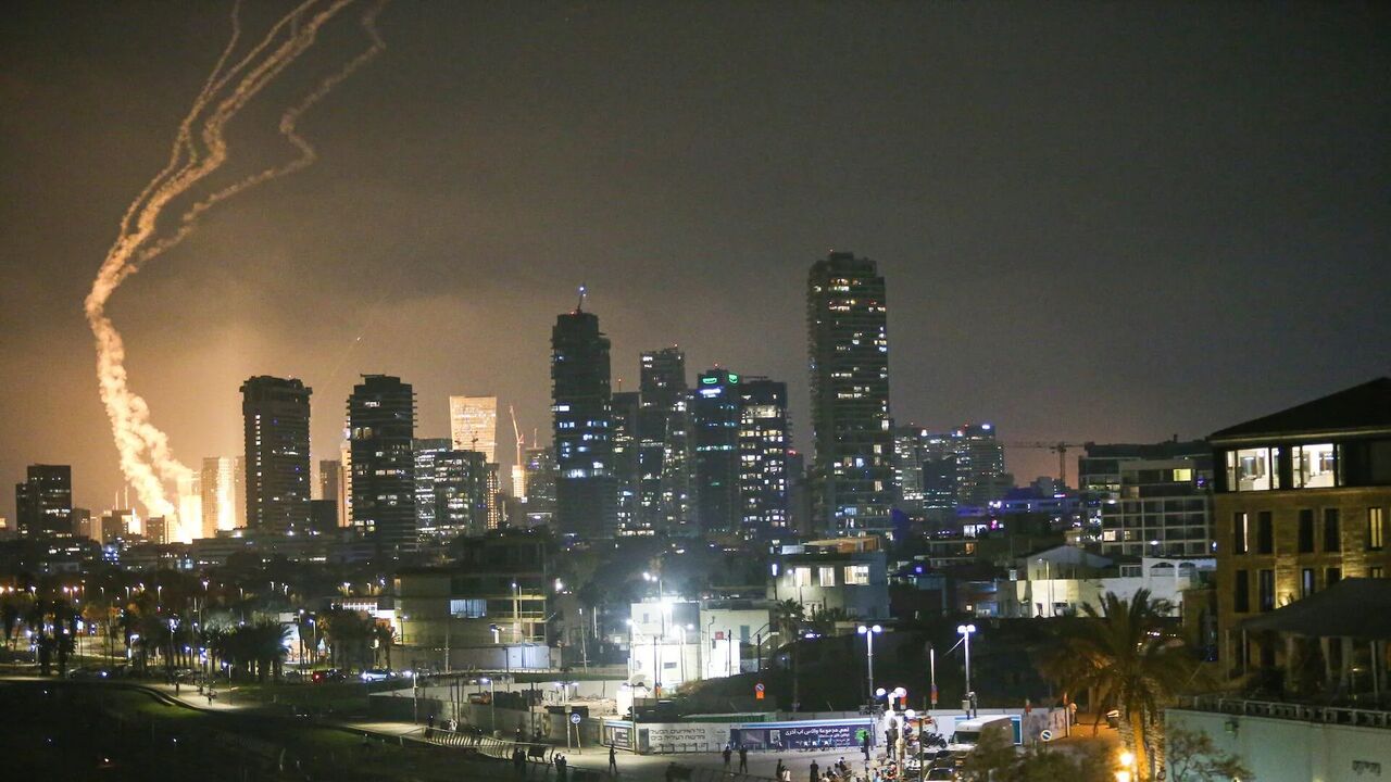 Rastros de foguetes no céu durante ataque noturno em meio aos prédios iluminados de Tel Aviv; conflito refletindo a escalada da Guerra Israel Irã.