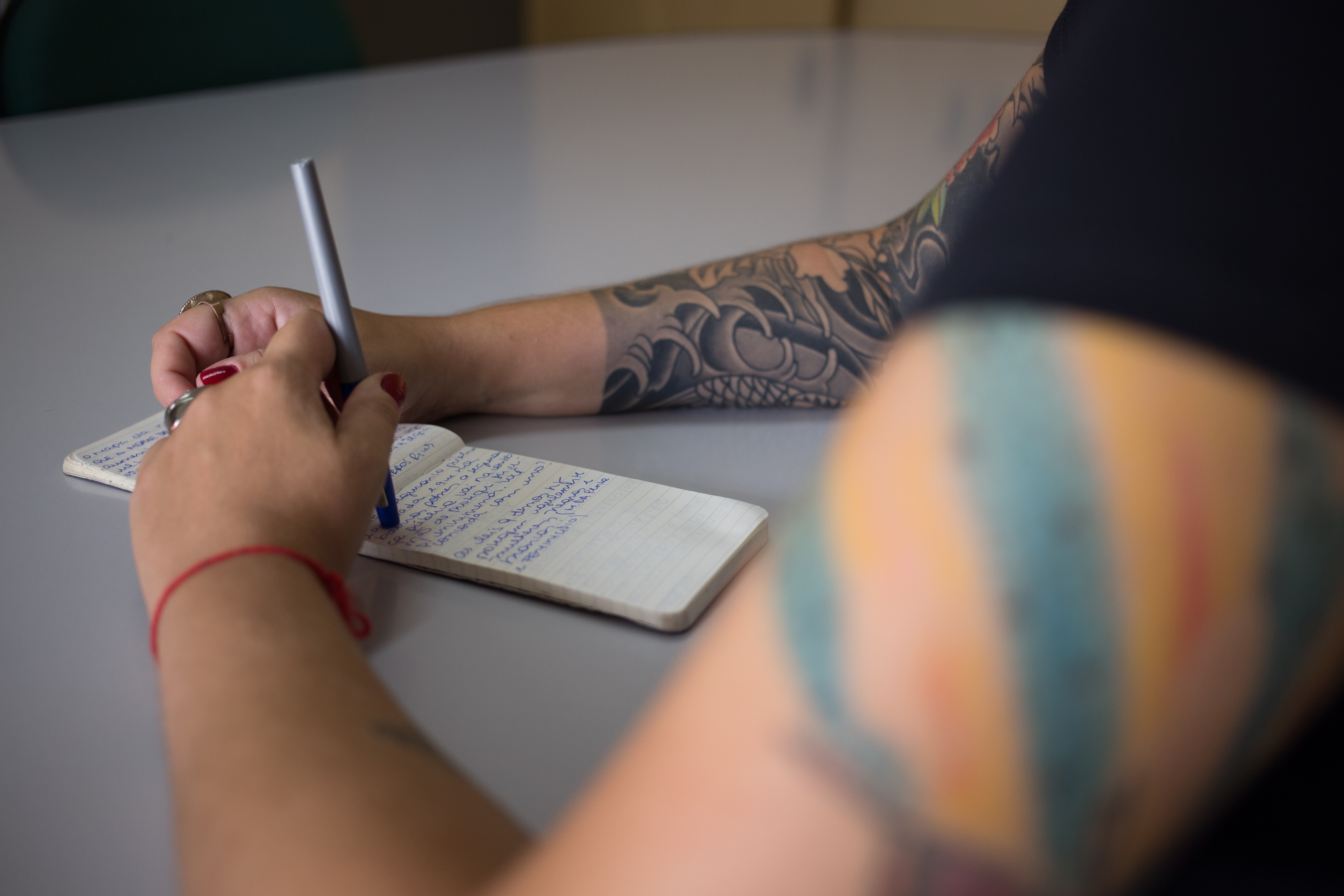 Pessoa tatuada escrevendo à mão em um caderno, representando o processo de criação de crônicas literárias